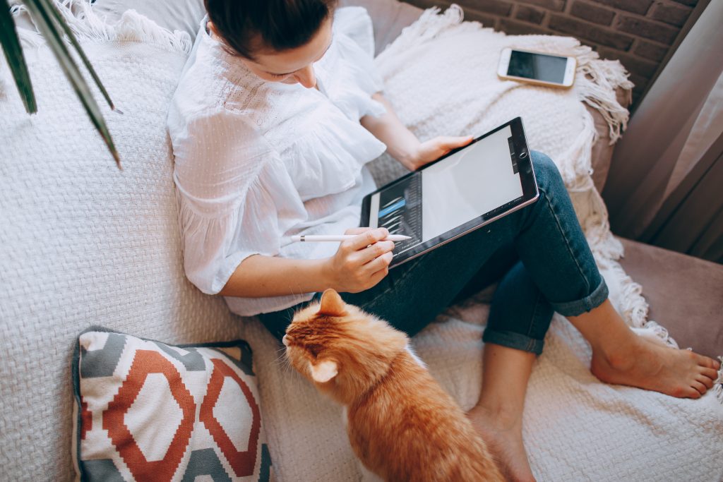 Woman sitting on a couch with her cat drawing on a tablet