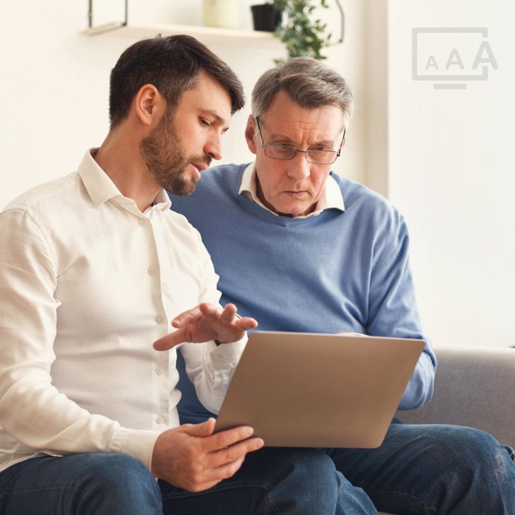 Two men, the younger is explaining something on a laptop to the older